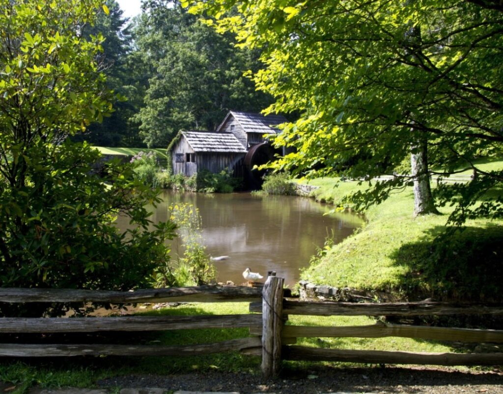 Blue Ridge Parkway Scenic View — RV USA road trip routes Scenic view of a pond with a rustic building and lush greenery along the Blue Ridge Parkway. — RV USA road trip routes
