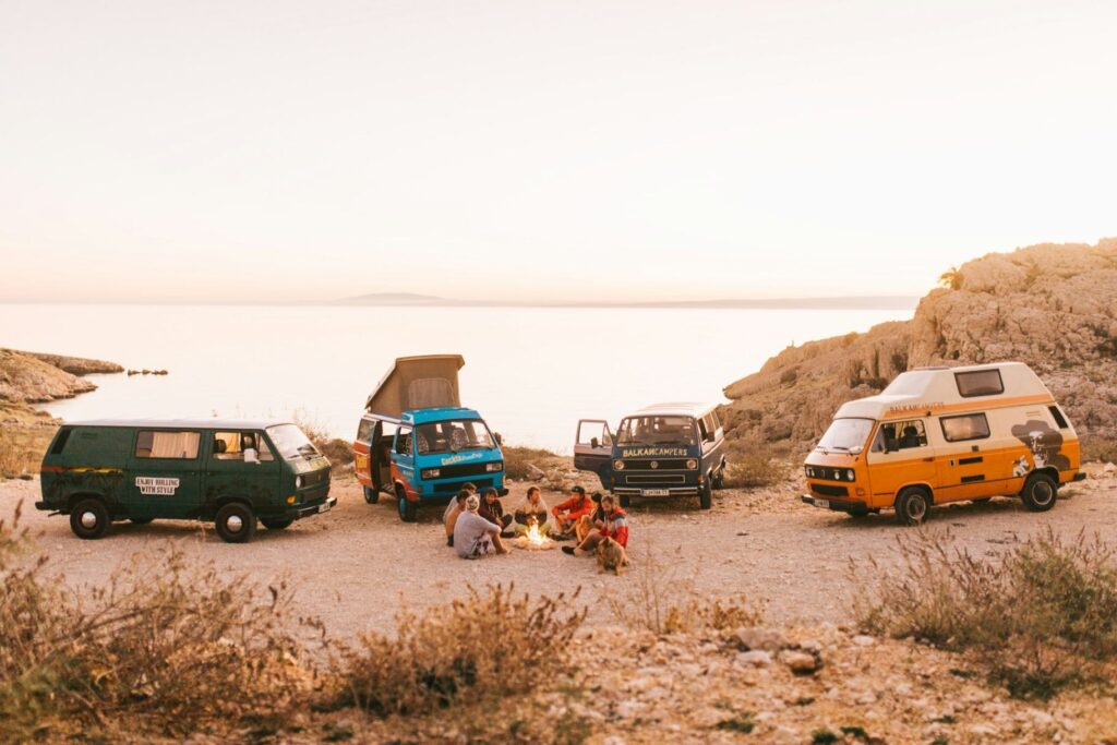 Camping on a Cross-Country Road Trip — USA cross-country road trip Group of people camping near vintage vans by the water at sunset. — USA cross-country road trip
