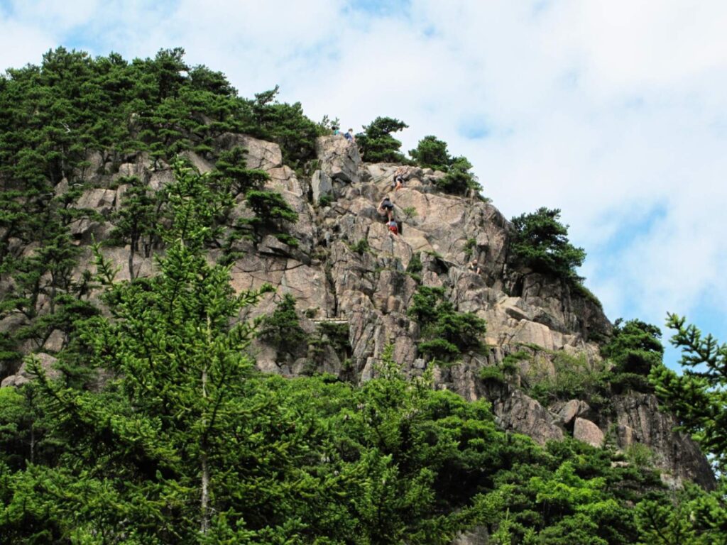 Climbers on Rocky Cliff — beautiful places in America to visit Climbers scaling a rocky cliff surrounded by lush green trees. — beautiful places in America to visit