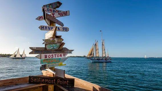 Directional Signpost at Key West — unique travel destinations in the USA Signpost with directional arrows pointing to various cities near the ocean with a — unique travel destinations in the USA