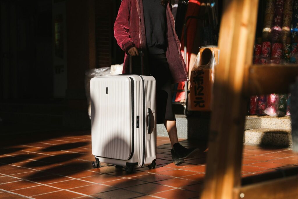 Traveler with Suitcase — Travel Essentials A traveler pulling a white suitcase in a sunlit area. — Travel Essentials