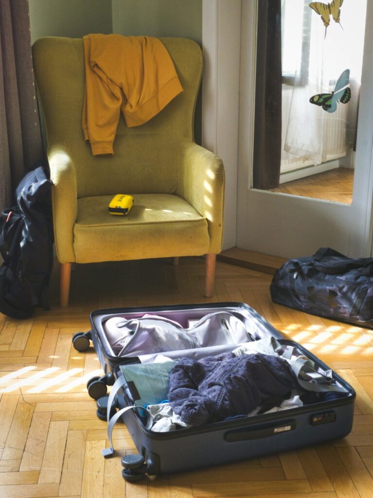 Packing Tips for Travelers — international travel tips for first-time A suitcase partially packed with clothes next to a chair and bags in a room. — international travel tips for first-time