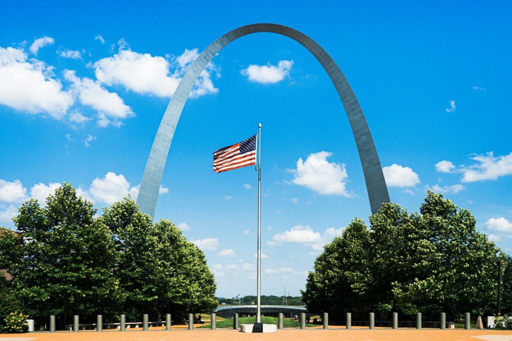 Gateway Arch in St. Louis — cheap places to travel in USA Arch tram at the Gateway Arch with American flag and trees — cheap places to travel in USA