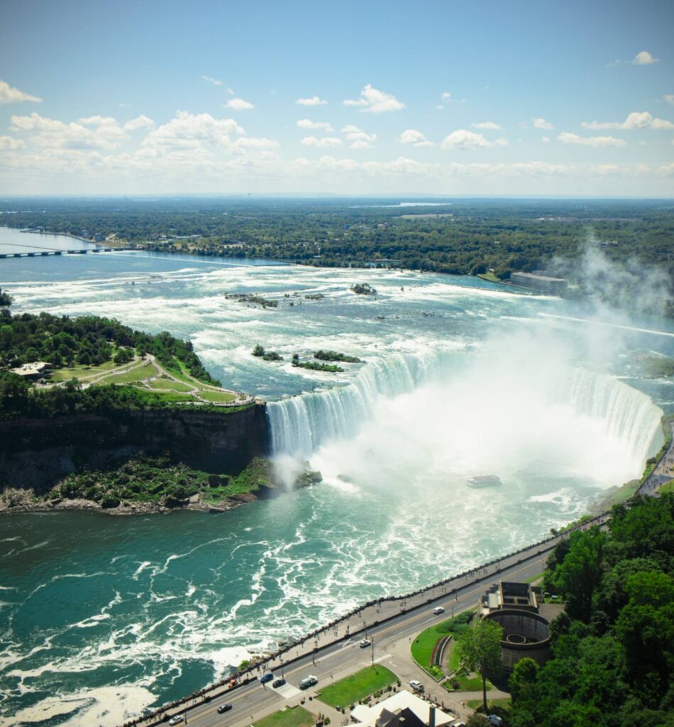 Niagara Falls Overview — beautiful places in America to visit Niagara Falls cascading into the river with lush greenery surrounding the area. — beautiful places in America to visit