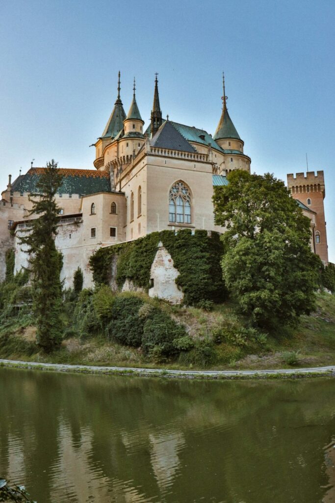 Bojnice Castle in Slovakia — places to visit in Slovakia Bojnice Castle reflected in the water with lush greenery around it. — places to visit in Slovakia