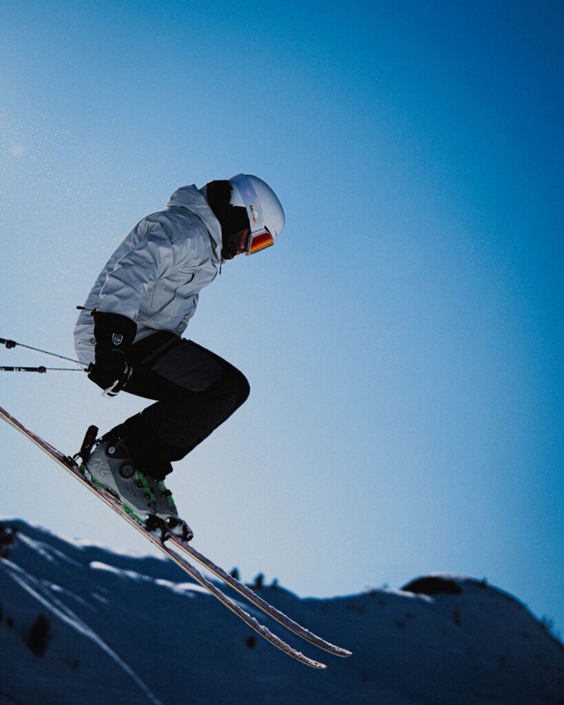 Skiing Action Shot — ski trip packing list Skier in white jacket jumping against a blue sky — ski trip packing list