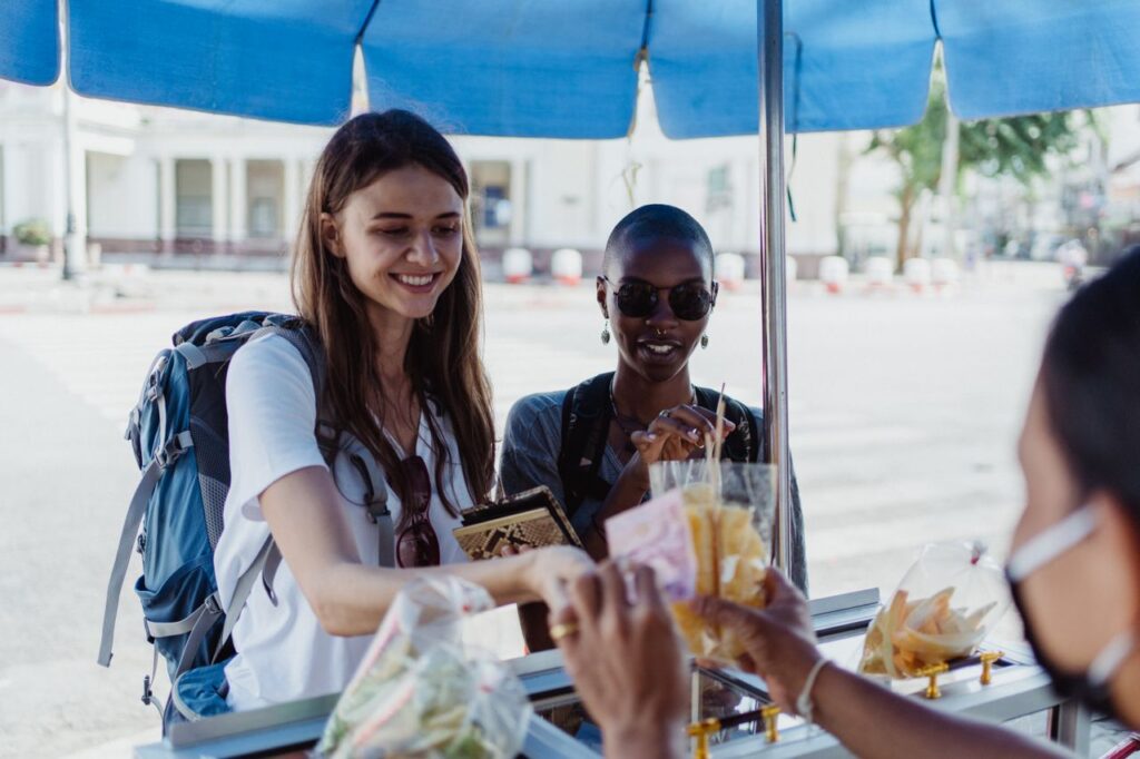 Budget Travel Tips: Eat Like a Local Two travelers enjoying street food at a local market. — Budget Travel Tips