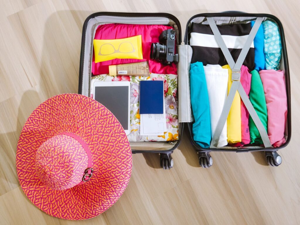 Travel Essentials Checklist Items Travel essentials checklist items packed in a suitcase with a hat and sunglasses.