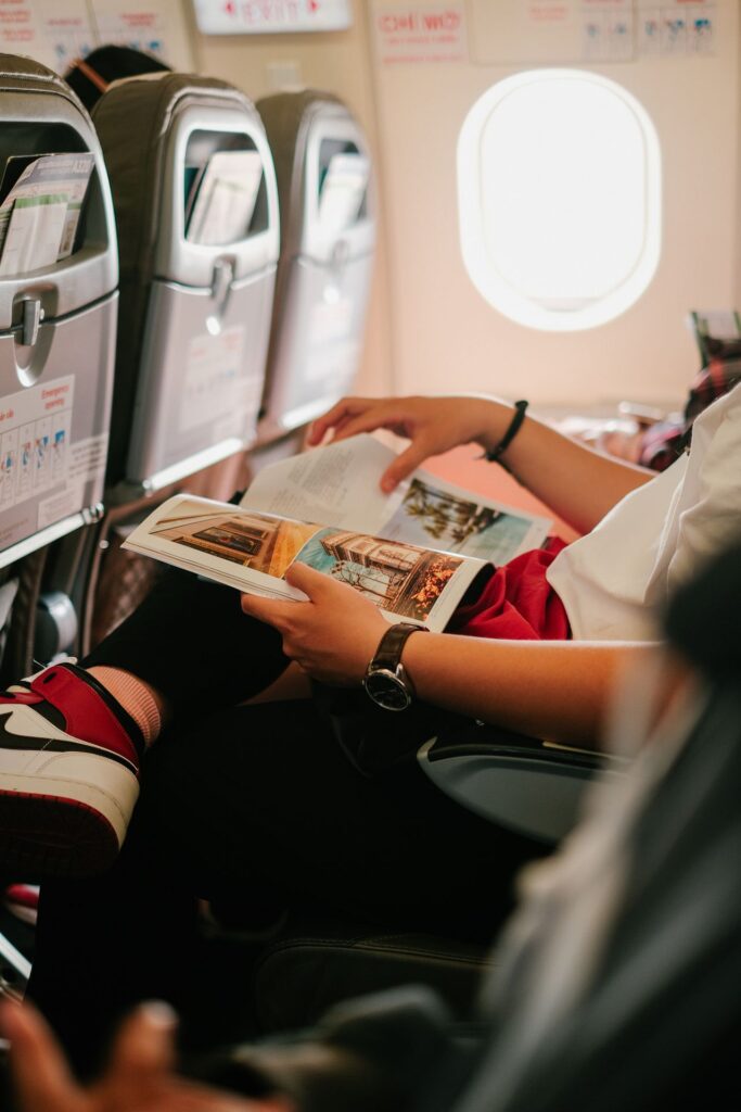 Airplane Travel Comfort Essentials — long flight comfort essentials Person reading a magazine on a plane during a long flight. — long flight comfort essentials