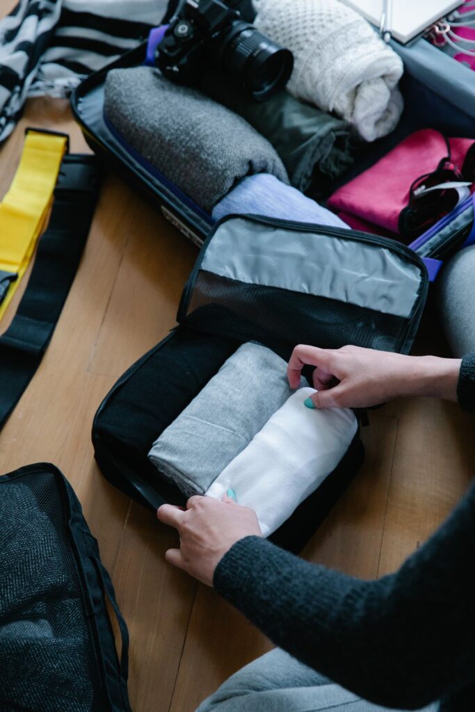 Packing Travel Essentials — travel essentials checklist Person packing a travel bag with rolled clothes and accessories. — travel essentials checklist