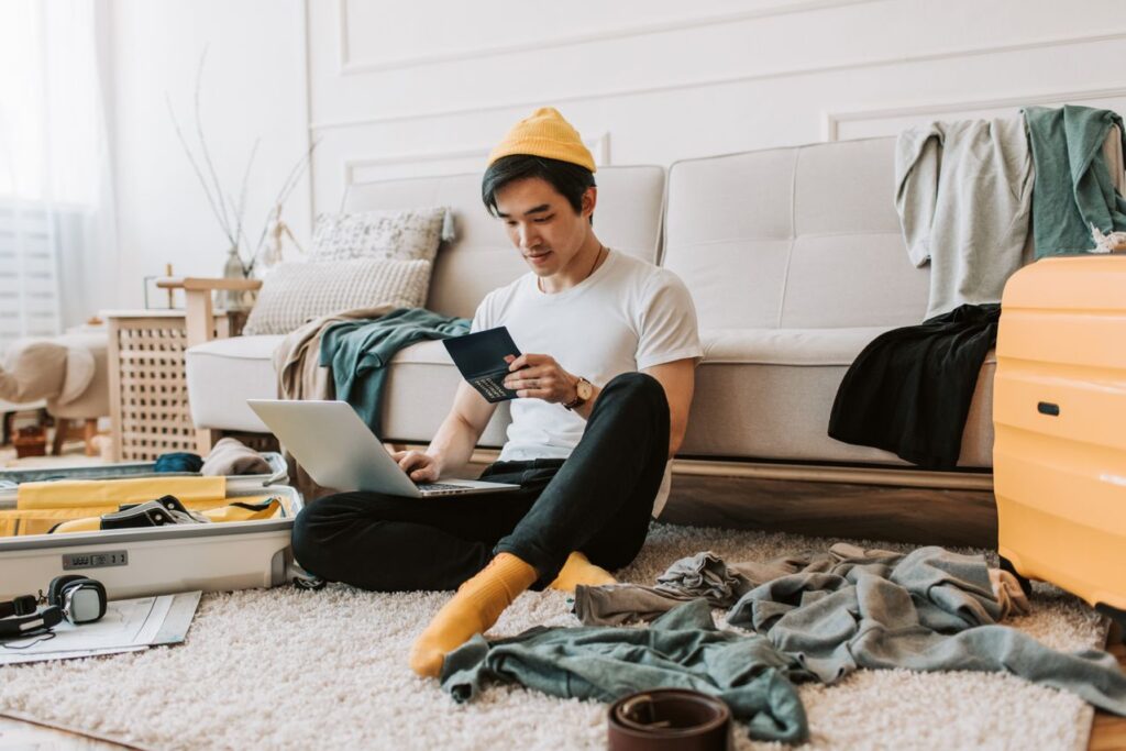 Packing Tips for Vacation — easier vacation planning tips Man planning a trip with a laptop and suitcase surrounded by clothes. — easier vacation planning tips