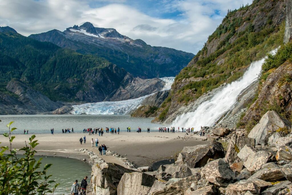 Glacier and Waterfall in Juneau — 7-day alaska cruise packing list Scenic view of a glacier and waterfall in Juneau, Alaska with people exploring the area. — 7-day alaska cruise packing list