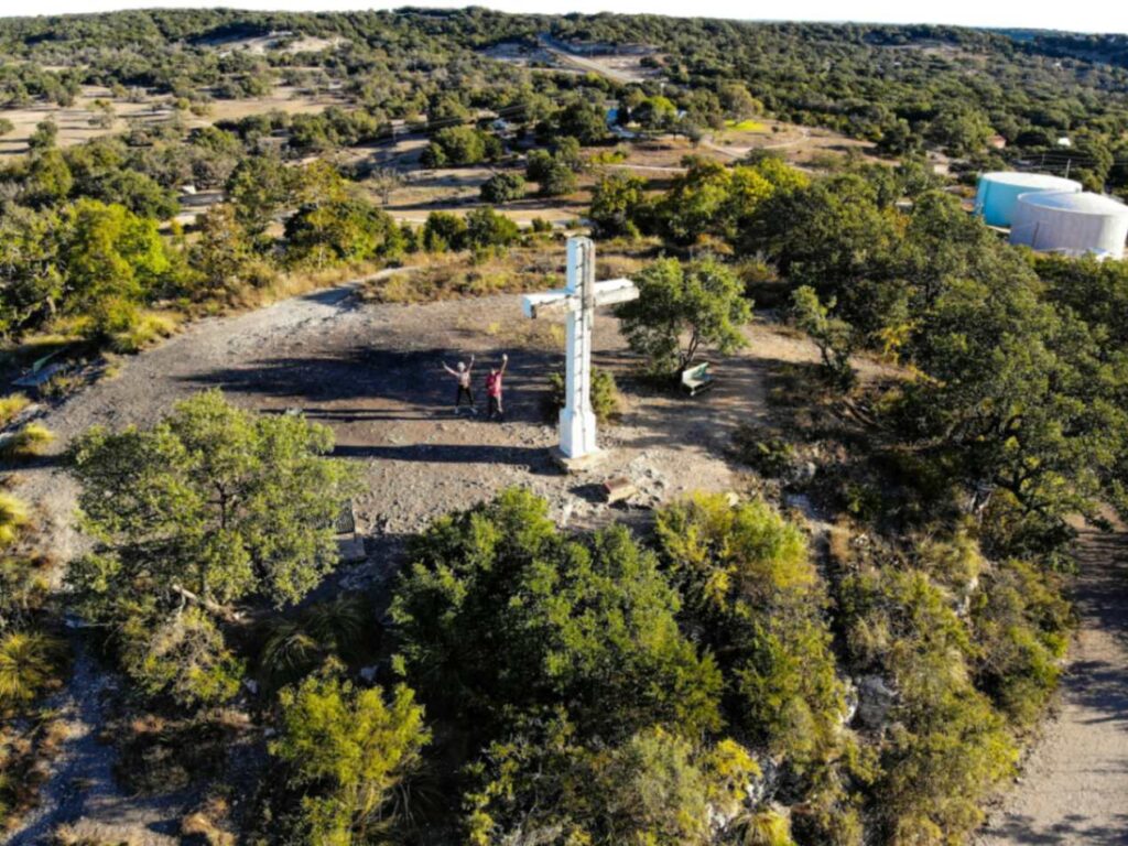 Rural Cross Surrounded by Nature — charming small towns in the USA Aerial view of a large white cross surrounded by trees and rocky terrain in a rural area. — charming small towns in the USA