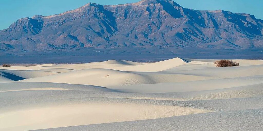 White Sands National Park Landscape — unique travel destinations in the USA Unique travel destinations in the USA featuring white gypsum dunes with distant mountains under a clear blue sky.