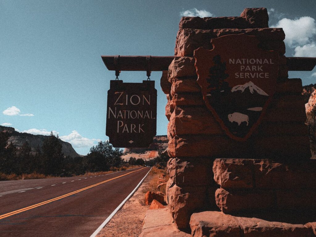 Zion National Park Entrance Sign — beautiful places in America to visit Entrance sign for Zion National Park along a scenic road under a blue sky — beautiful places in America to visit